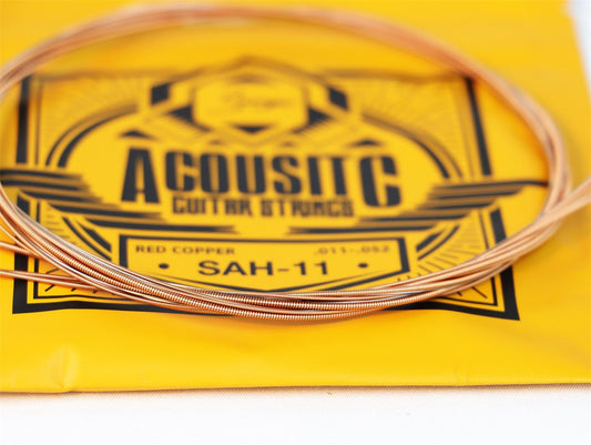 Acoustic guitar string set on a yellow background with branding.