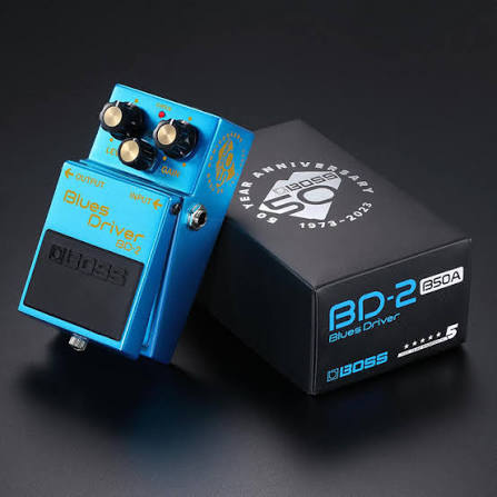 A blue Boss Blues Driver 50th Anniversary BD-2 G50A guitar effects pedal shown next to its black retail box on a dark studio background.